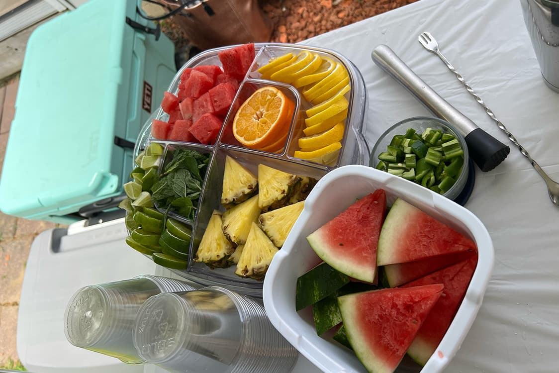 Trays of fresh-cut watermelon, pineapple, citrus, and cucumber prepared for the bar