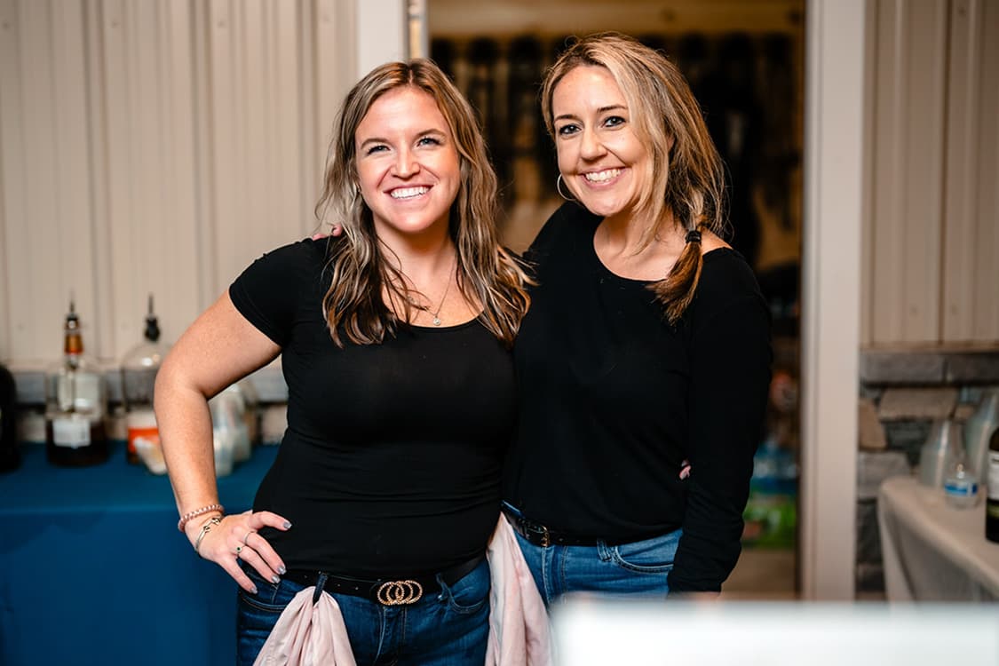 Kayla and a teammate in black shirts standing behind an event bar